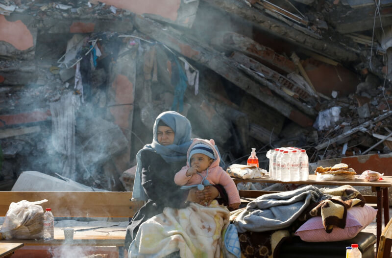 土耳其強震後，10日哈泰省一名婦女抱著孩子坐在倒塌的建物旁。（路透社）