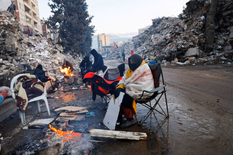 土耳其卡拉曼瑪拉斯省災情慘重，民眾13日坐在倒塌的建物旁生火取暖。（路透社）