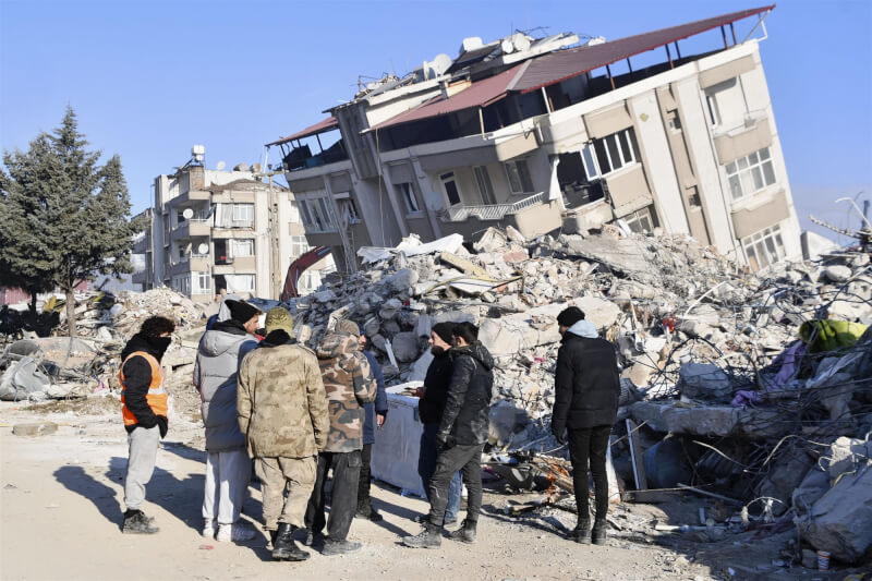 圖為10日土耳其安塔基亞民眾站在傾斜倒塌的房屋前。（共同社）