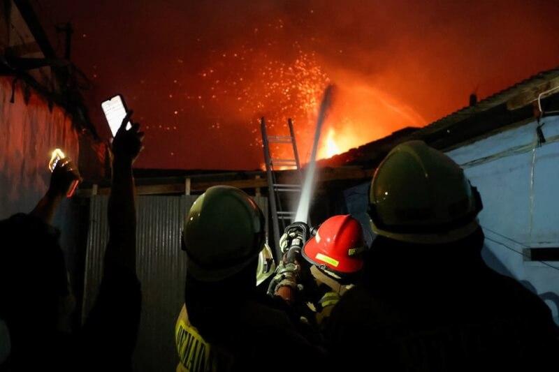 印尼國營石油公司一座油庫爆炸火勢延燒民宅，消防人員灑水灌救。（路透社）