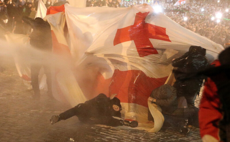 圖為喬治亞民眾3月走上首都特比利西街頭抗議政府推出爭議的外國代理人法案，遭警方噴灑水柱驅趕。（路透社）