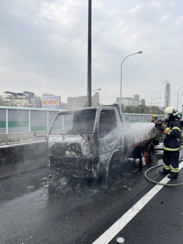 國道1號北向356.3公里高雄楠梓段8日上午發生火燒車意外，一輛自小貨車行進間突然起火燃燒，緊急停到路肩，所幸車上2人順利逃生均無受傷；消防人員獲報前往撲滅火勢。（國道公路警察局提供）中央社記者洪學廣傳真 112年4月8日