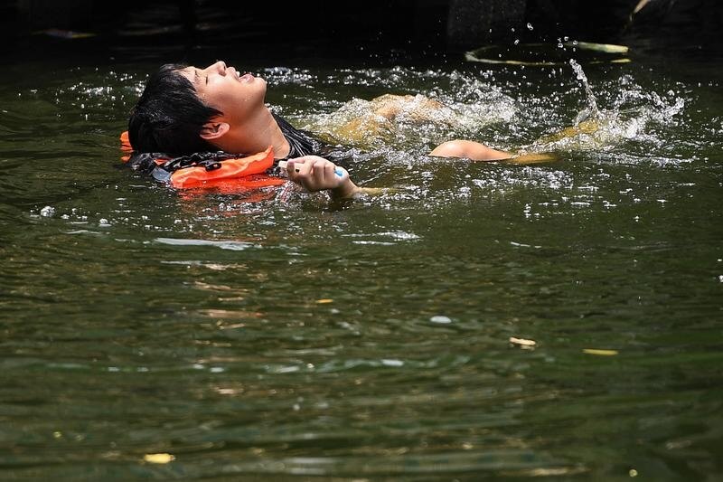 圖為22日一名男子在曼谷一處運河游泳。（路透社）
