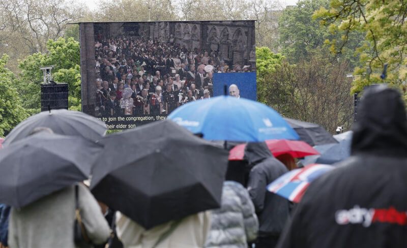 查爾斯三世6日加冕儀式時，倫敦天空飄著雨，民眾撐傘在公園觀看加冕儀式的直播畫面。（共同社）