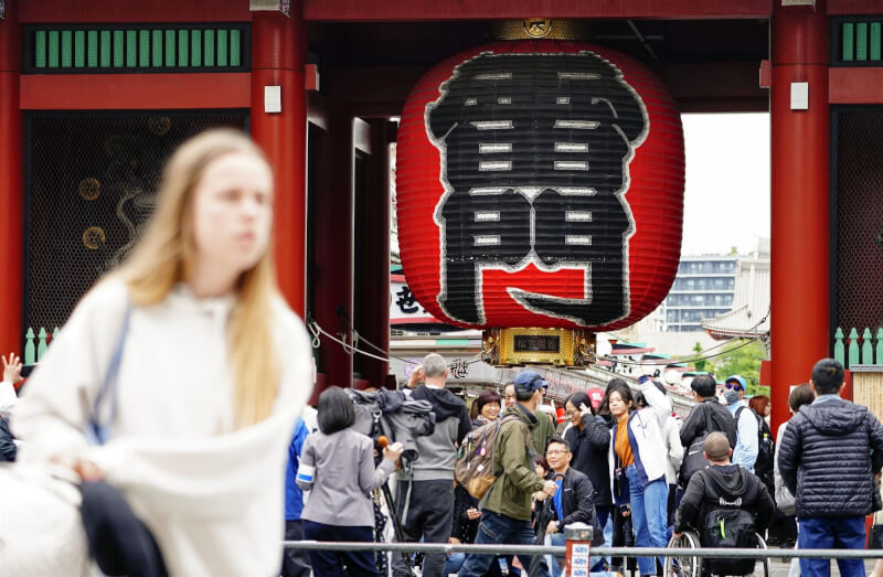 日本8日將COVID-19降級為等同季節性流感的第5類傳染病。圖為東京淺草寺雷門前遊客脫下口罩合影。（共同社）