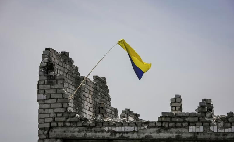 圖為路透社記者去年6月進入烏克蘭的涅斯庫奇涅村，看到烏國國旗在破敗雜貨店上方飄揚。（路透社）