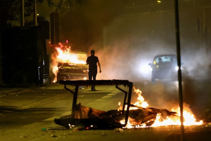 法國暴動持續，圖為民眾站在燃燒的車輛旁。（路透社）