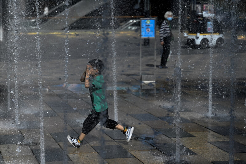 圖為北京一名男孩跑過噴水的噴泉消暑。（法新社）