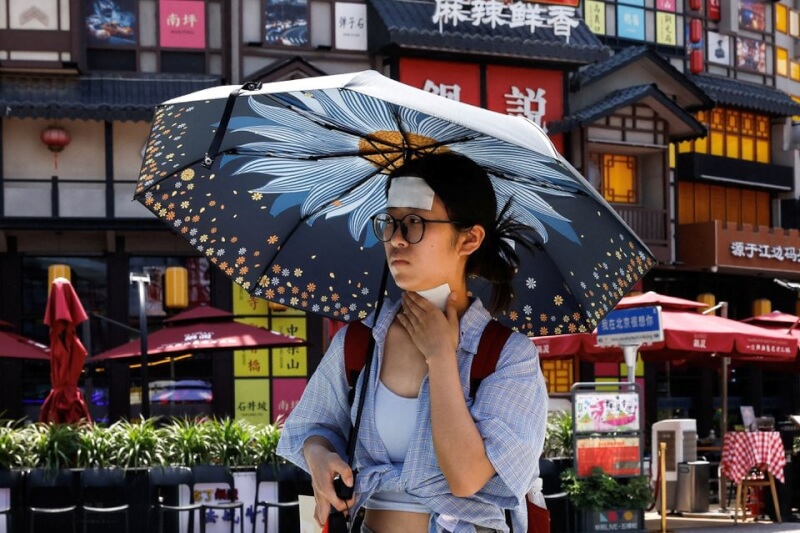 圖為中國北京女子撐陽傘走在路上。（路透社）