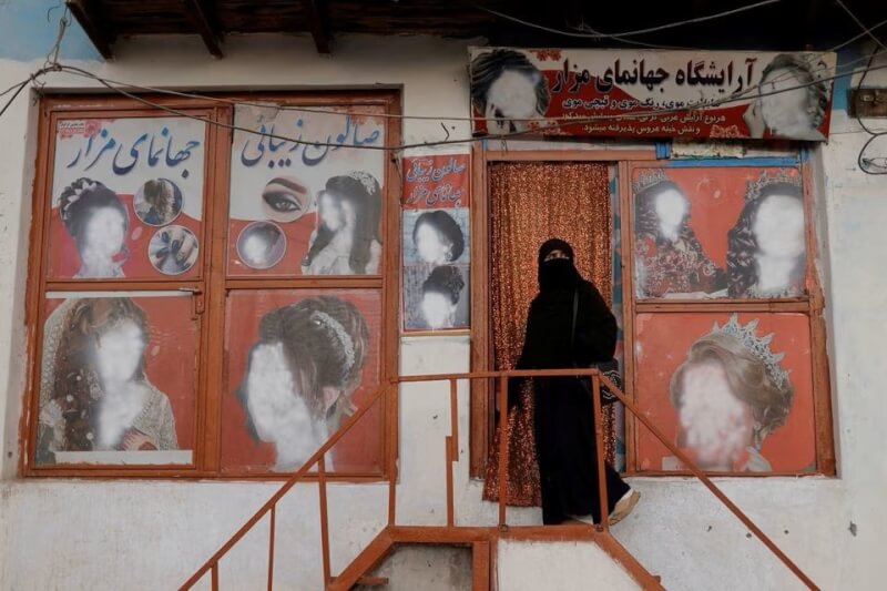 阿富汗塔利班政權的「勸善懲惡部」4日證實，全國各地的美容院須在一個月內關閉。圖為一名阿富汗女性走入美容沙龍，牆外的女性面容都已遭抹除。（路透社）