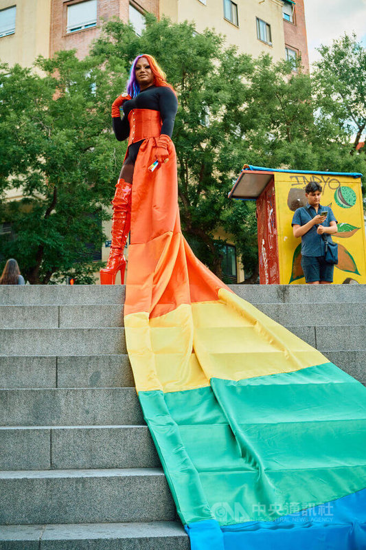 7月1日馬德里「驕傲大遊行」下午，有裝扮皇后利用捷運站入口的樓梯，展開以彩虹大旗做成的裙子，擺起姿勢拍照。中央社記者胡家綺馬德里攝  112年7月6日