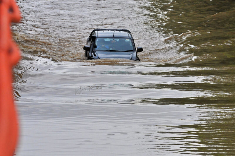 圖為9日印度古爾岡汪洋一片，民眾在被洪水淹沒的道路駕駛車輛。（法新社）