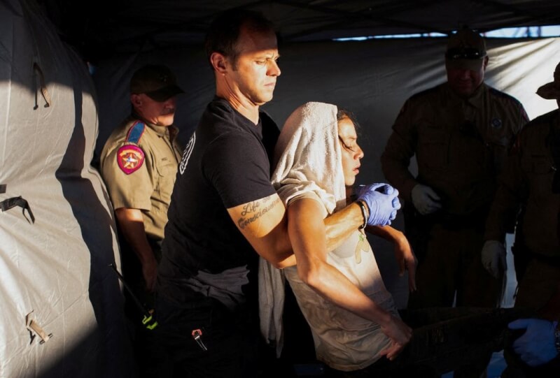 圖為6月26日，德州消防員將一名中暑的移民抬上擔架。（路透社）