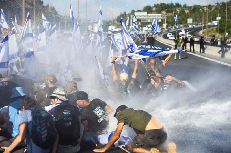 以色列國會11日一讀通過司法改革計畫中一項重要議案，數小時後全國各地爆發抗議活動。圖為抗議群眾11日封鎖通往耶路撒冷的高速公路，警方以高壓水炮驅離。（路透社）