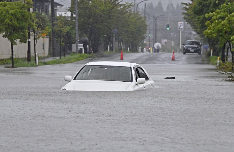 日本秋田縣降下破紀錄大雨，15日有汽車被困在淹水的道路中。（共同社）