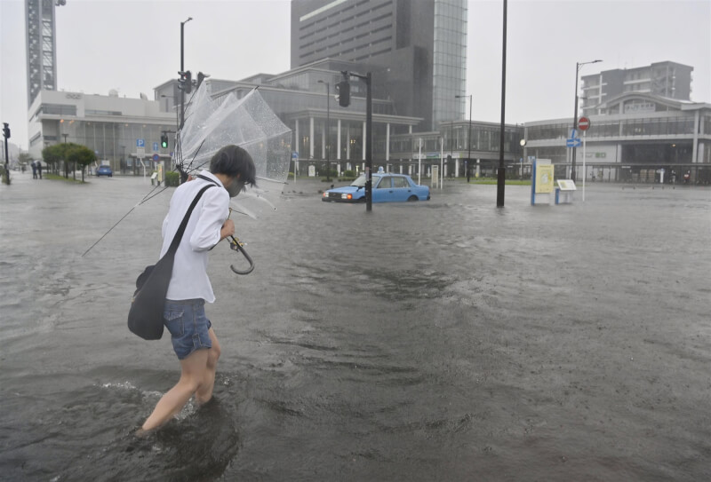 大雨釀成JR秋田站前淹水，15日有民眾撐著壞掉的傘走在積水的道路中。（共同社）