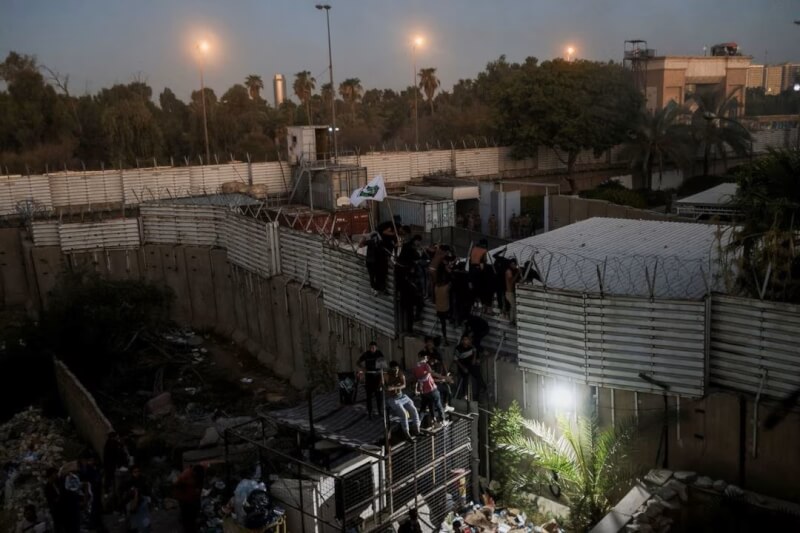 伊拉克民眾20日爬到瑞典駐巴格達大使館附近的圍牆上抗議。（路透社）