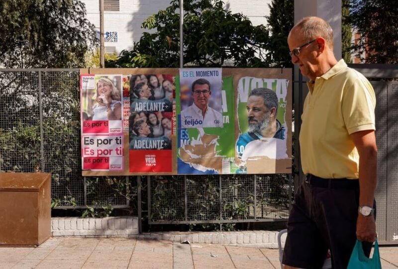 圖為西班牙一處街頭貼滿競選海報，一名男子7日行經而過。（路透社）