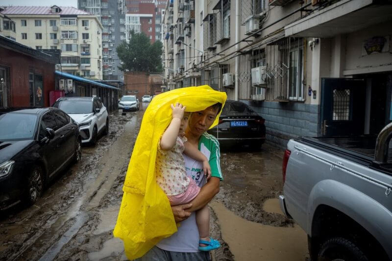 圖為北京一名男子抱著小孩走在洪水後泥濘的路上。（路透社）