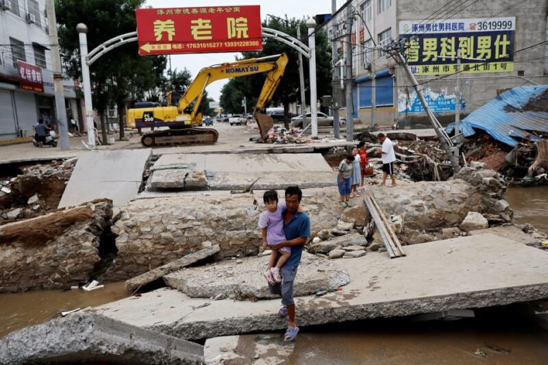 圖為河北省涿州一名男子在洪災後，抱著孩子走過受損的橋樑。（路透社）