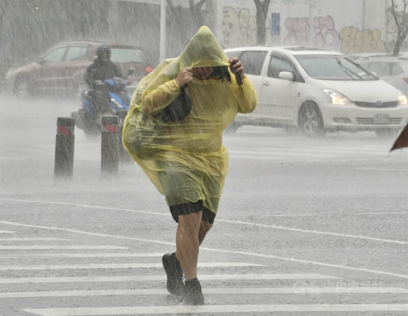 圖為高雄市新興區民眾穿著輕便雨衣、拉緊帽子在大雨中過馬路。（中央社檔案照片）