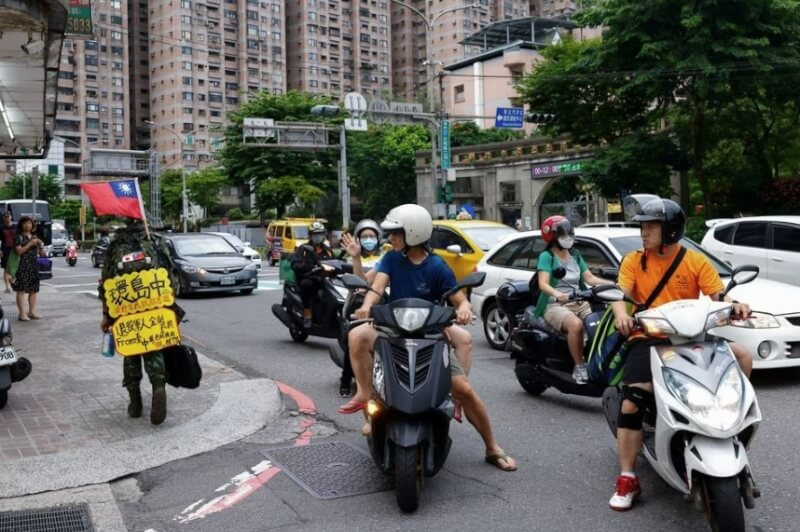 蔡宗霖的背包上插著一面國旗，上面還掛著一塊黃色牌子寫著「環島中，提升全民抗敵意識」。（路透社）