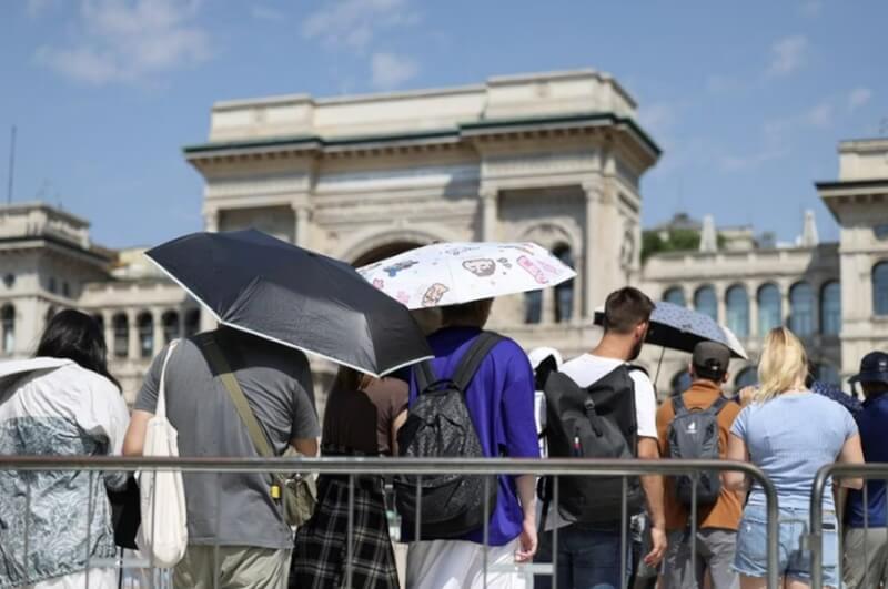 義大利米蘭高溫，遊客21日在大太陽下撐傘，排隊等待參觀教堂。（路透社）