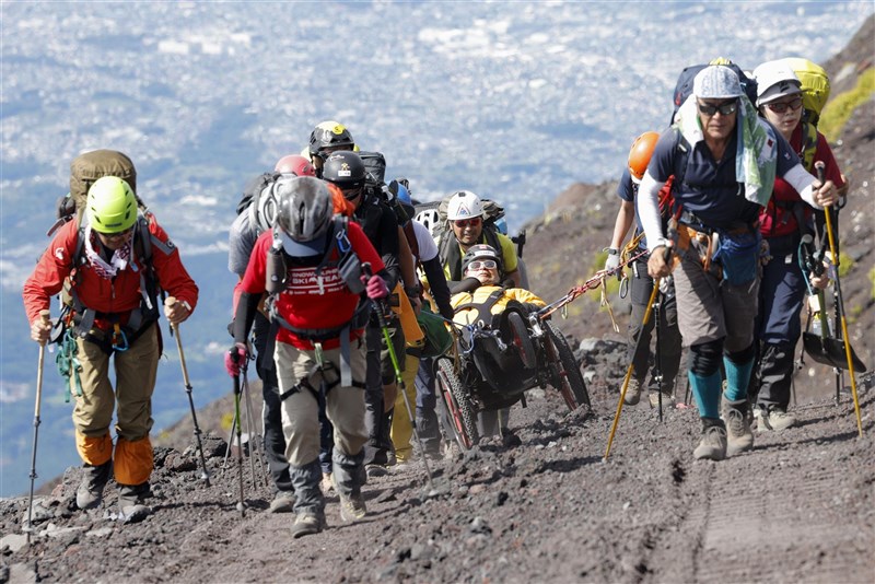 冒險家三浦雄一郎（中）親友協助下坐登山用輪椅攻頂。（共同社）