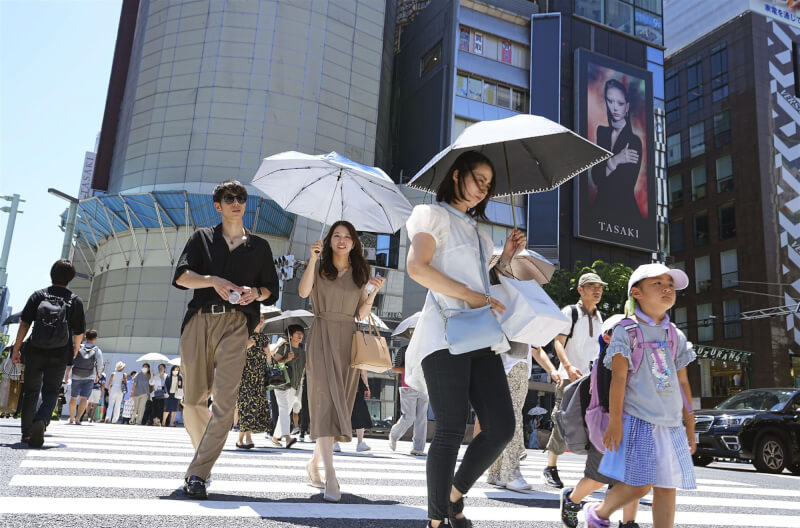 圖為東京銀座民眾撐傘在烈日下走動。（共同社）