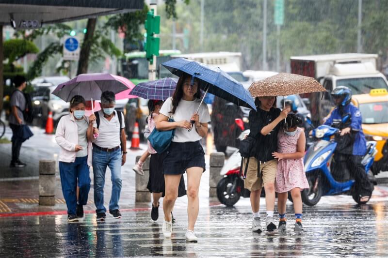 中央氣象局表示，未來一週低壓帶漸遠且減弱，各地降雨趨緩。圖為台北市信義區出現陣雨，民眾撐傘快步過馬路。（中央社檔案照片）