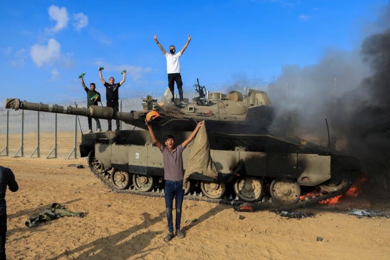 圖為以色列一輛軍車7日被巴勒斯坦槍手擊中後起火，巴勒斯坦人歡呼慶祝。（路透社）