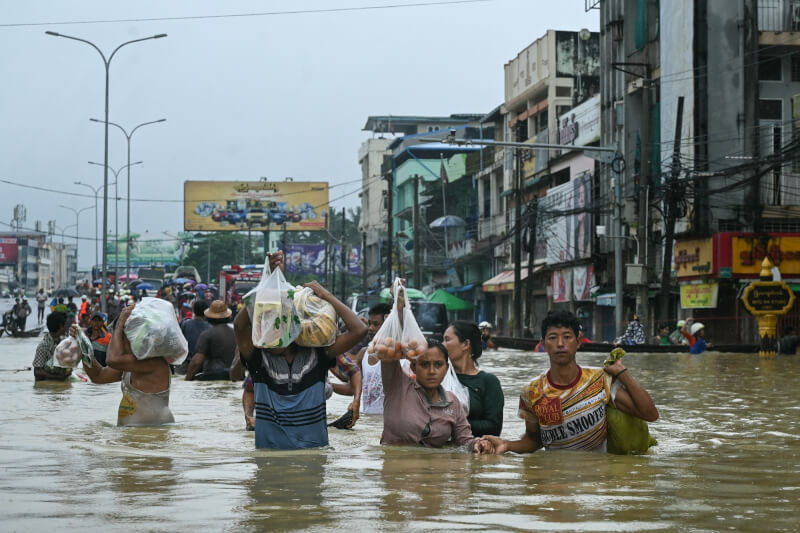 緬甸商業大城仰光附近城鎮勃固近日降雨量創新紀錄，圖為居民10日高舉著食物走在被洪水淹沒的街道。（法新社）