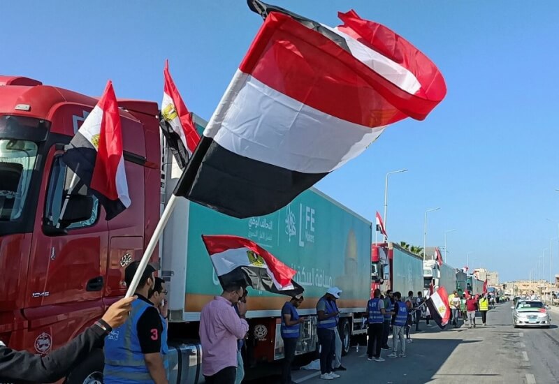 圖為插著埃及國旗的人道援助物資車隊15日堵在埃及接壤加薩走廊邊界附近，車隊周圍也有民眾舉著埃及國旗。（路透社）