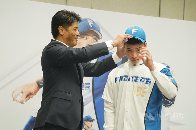 台灣18歲強投孫易磊(右)16日在台北出席加盟日本職棒北海道日本火腿鬥士隊記者會,火腿隊總經理稻葉篤紀(左)替孫易磊穿上球衣、球帽。中央社記者徐肇昌攝 112年10月16日
