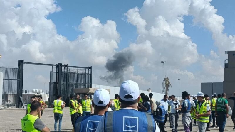 埃及志工17日等待拉法關卡重新開放，遠方可見以巴戰火硝煙。（路透社）