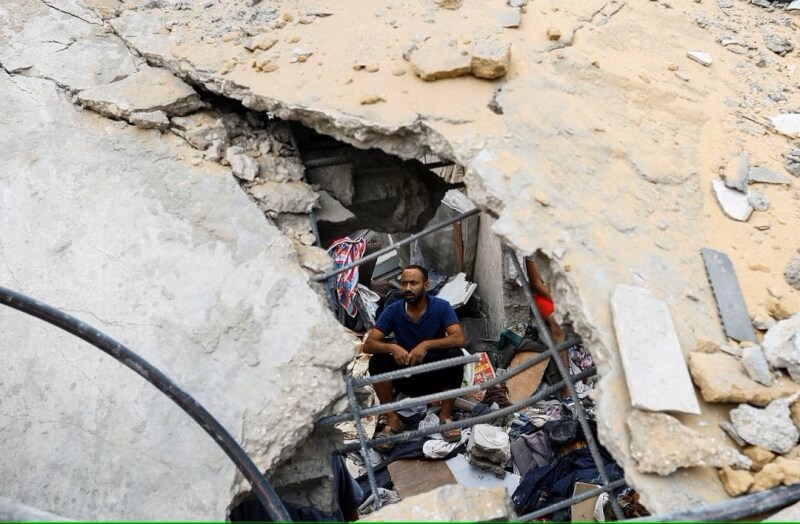 29日加薩走廊南部民眾坐在被砲擊後的廢墟中。（路透社）