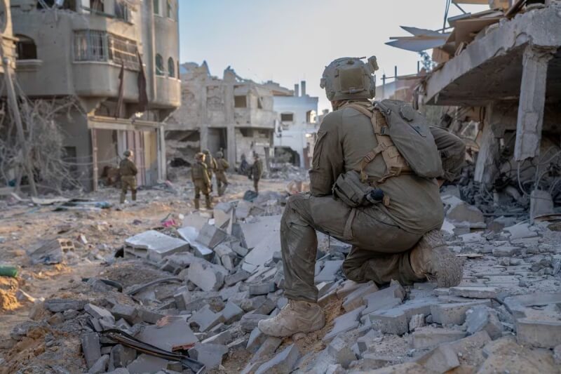 以色列部隊人員11日行經加薩走廊內遭空襲毀壞建物群。（Israeli Defense Forces/Handout via 路透社）