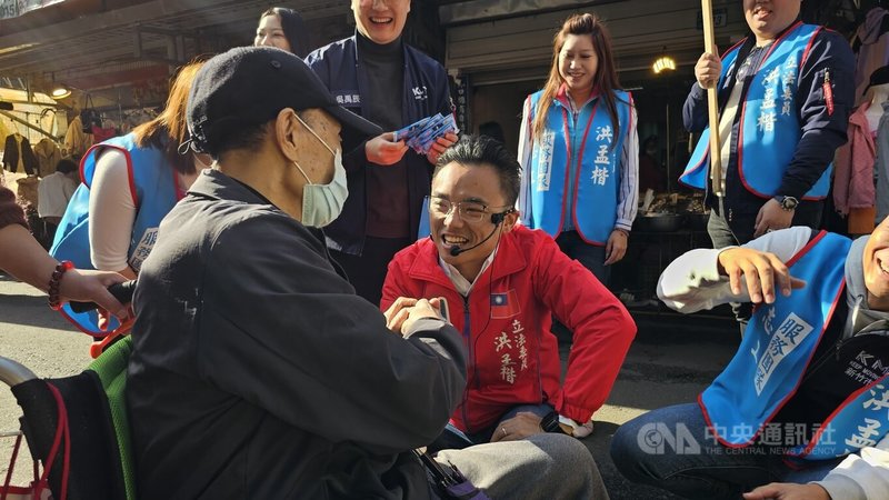 國民黨新北市立委參選人洪孟楷（中，紅衣）7日至林口的市場掃街拜票，受到不少攤商及民眾歡迎，還有坐輪椅的老翁向洪孟楷加油打氣。中央社記者王鴻國攝  112年12月7日