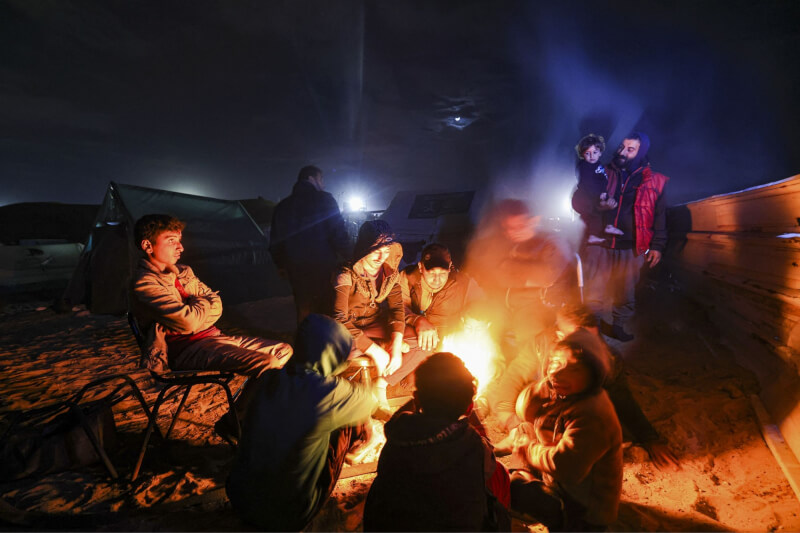 流離失所的加薩人14日在拉法一個臨時營地取暖。（法新社）