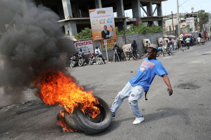 圖為7日海地太子港，1名男子在抗議現場踢著燃燒的輪胎。（路透社）