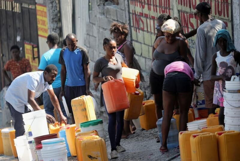 圖為12日海地民眾拿著水桶排隊取水。（路透社）