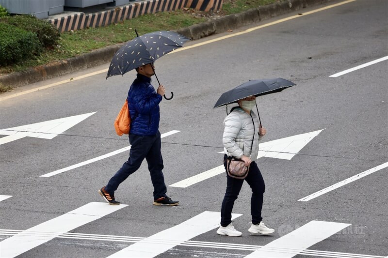 圖為台北市士林區，民眾穿上羽絨外套、撐傘過馬路。（中央社檔案照片）