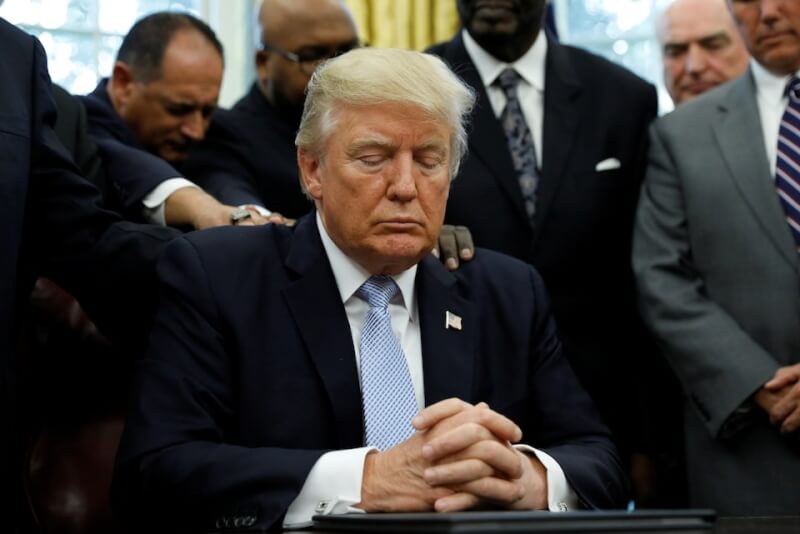 時任美國總統川普2017年9月1日坐在白宮橢圓形辦公室，宗教領袖將手川普肩上，為因颶風哈維受難的人們祈禱。（路透社）