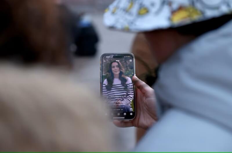 圖為22日英國倫敦白金漢宮外，民眾正透過手機觀看凱特王妃宣布自己罹患癌症的消息。（路透社）