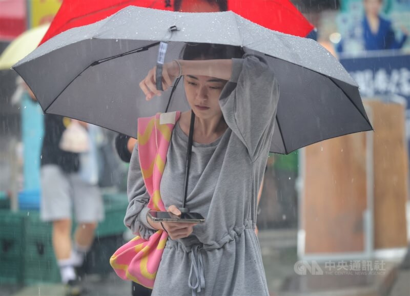 圖為台北市中午下起大雨，走在信義區街頭的民眾撐傘遮雨。（中央社檔案照片）