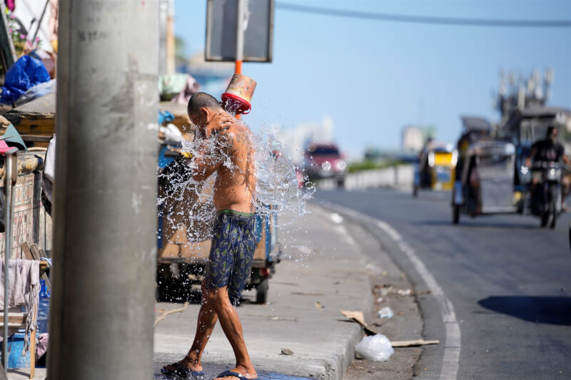 菲律賓近日受極端高溫考驗，首都馬尼拉市區路邊一名男子沖水納涼。（美聯社）
