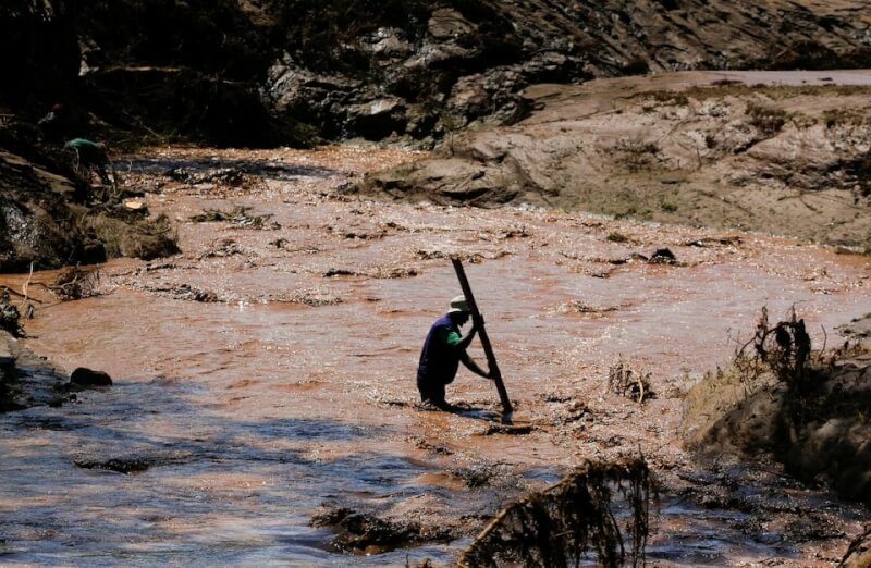 肯亞南部水壩潰堤後，1名男子手持木棍渡河。（路透社）