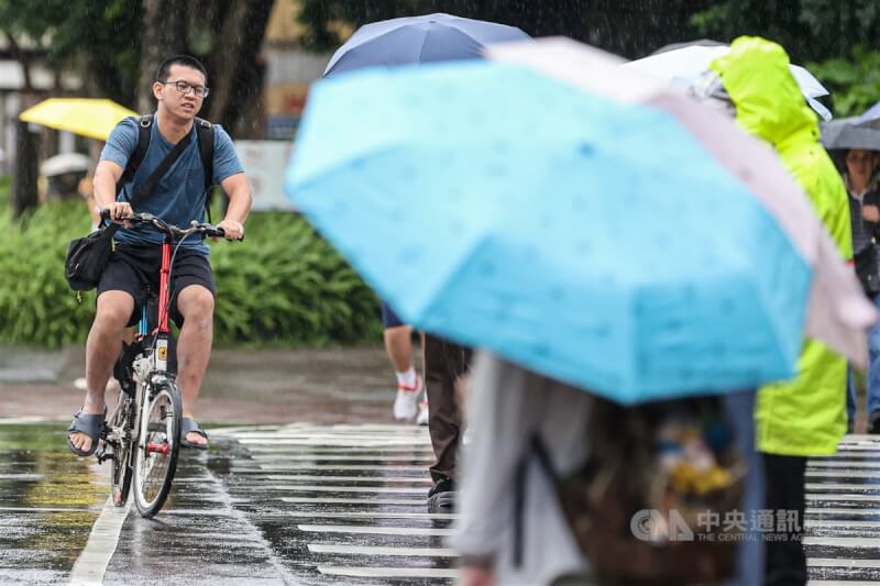 台北市區民眾紛紛撐傘遮擋雨勢，有人冒雨騎自行車，快速通過馬路。（中央社檔案照片）