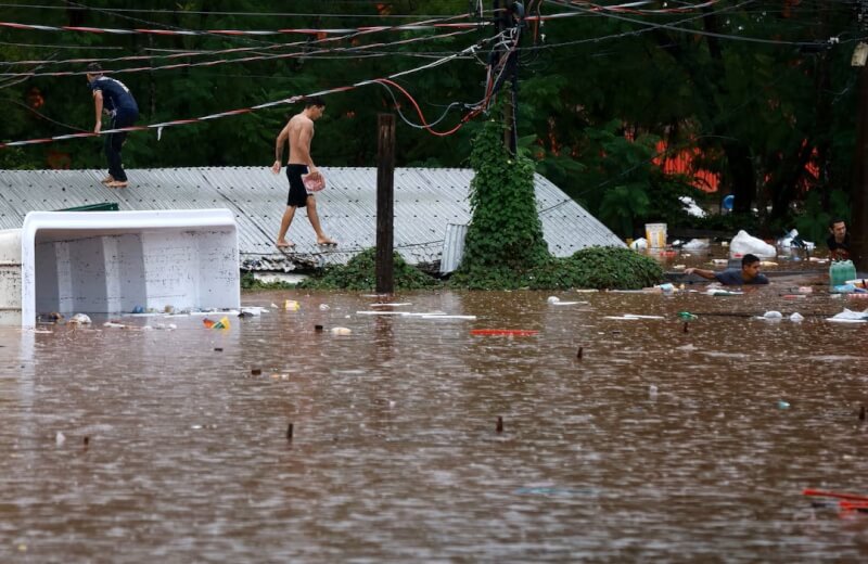 巴西南大河州暴雨後，2日民眾在被洪水淹沒地區的屋頂上行走。（路透社）