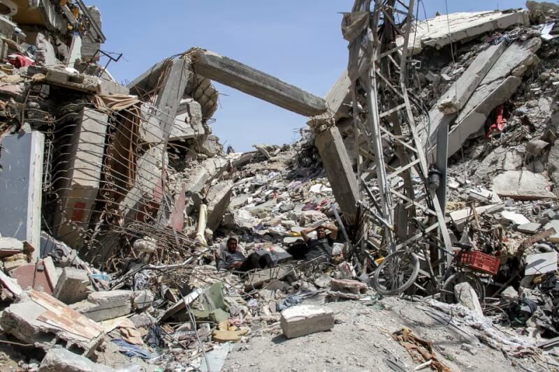 圖為4月22日加薩走廊可見巴勒斯坦民眾坐在一處遭以色列炸毀的建築廢墟中。（路透社）